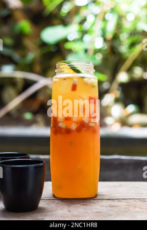 Flasche mit frischem, hausgemachtem Saft aus Orangen, Wassermelone, Limette auf dem Holztisch mit Tassen Stockfoto