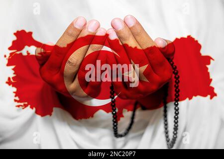 Eine muslimische Frau erhebt ihre Hände, um zu beten. Unterstützung und Gebete für Erdbebenopfer in der Türkei. Mond und Sterne stehen für die Flagge der Türkei. Stockfoto