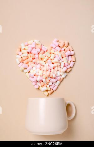 Tasse und Herz aus Marshmallow auf beigefarbenem Hintergrund, flach liegend Stockfoto