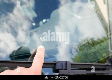 Finger-Hand-Mann zeigt auf die kaputte Windschutzscheibe eines Autos, Spuren von entgegenkommenden Steinen auf der Straße Stockfoto