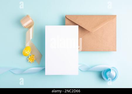 Ästhetische Osterkomposition. Leere Karte, Ostereier, wunderschöne bunte Bänder und Umschlag auf pastellblauem Hintergrund, Kopierbereich. Stockfoto