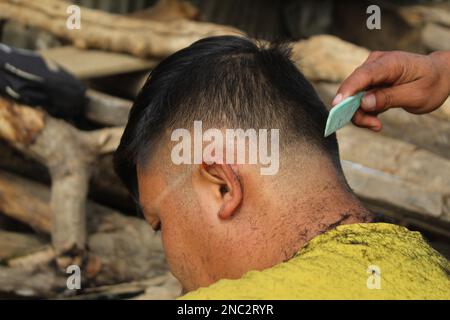 Meister schneidet im Friseursalon Haare und Bart von Männern, Friseur macht Frisuren für einen jungen Mann im Hintergrund von Fleck Stockfoto