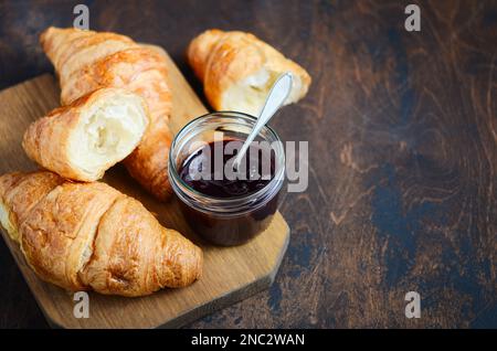 Frisch gebackene Croissants mit Marmelade auf dunklem Holzhintergrund. Stockfoto