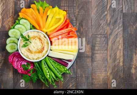 Hummus-Platte mit gemischten Gemüsesnacks. Gesunde vegane und vegetarische Speisen. Draufsicht, flach liegend, Kopierbereich. Stockfoto