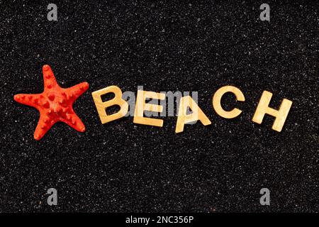 Strand: Goldene Buchstaben in schwarzem Sand und rote Seesterne Stockfoto