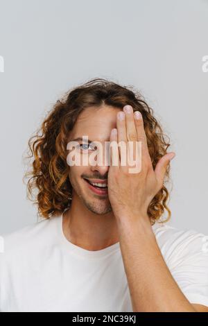 Ingwer-europäer mit lockigem, lächelndem Haar, der sein Auge verdeckt, isoliert auf weißem Hintergrund Stockfoto