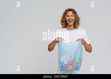 Ein Mann aus ingwereuropa, der ein lächelndes T-Shirt trägt, während er eine Plastiktüte hält, deren Müll auf weißem Hintergrund isoliert ist Stockfoto