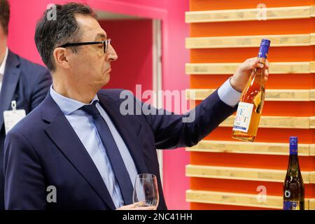 Nürnberg, Deutschland. 14. Februar 2023. Bundesminister für Landwirtschaft, Cem Özdemir (M, Bündnis 90/die Grünen), schaut auf einer Tour durch die Biofach-Messe auf eine Flasche Bio-Wein Rose. Vom 14. Bis 17. Februar 2023 präsentieren 2.765 Aussteller aus 95 Ländern auf der weltweit führenden Fachmesse für Bio-Lebensmittel Biofach und der Fachmesse für Naturkosmetika VIVANESS Produkte der Bio-Lebensmittel- und Naturkosmetikindustrie. Kredit: Daniel Karmann/dpa/Alamy Live News Stockfoto