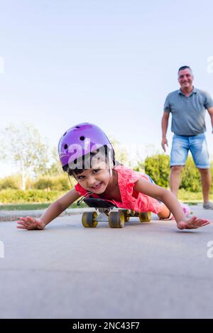 Ein Mädchen, das mit seinem Vater spielt, während es im Park Rollschuhlaufen geht. Stockfoto