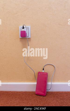 Mobiltelefon auf dem Boden mit angeschlossener pinkfarbener Tasche und Aufladen mit pinkfarbenem USB-Stecker und Kabel. Konzept: Frauen und Technologie, weibliches Telefonzubehör Stockfoto