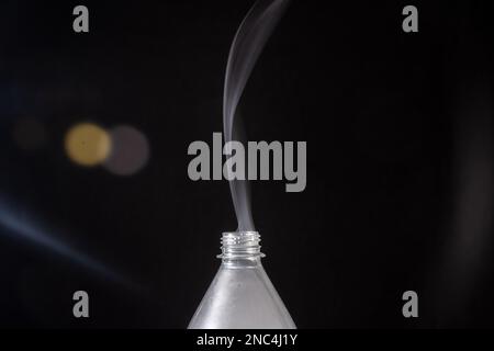 Rauch tritt aus einer Plastikflasche vor schwarzem Hintergrund mit Lichtreflexionen aus. Konstruktionselement. Stockfoto