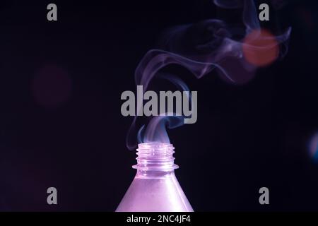 Rauch tritt aus einer Plastikflasche vor schwarzem Hintergrund mit Lichtreflexionen aus. Konstruktionselement. Stockfoto