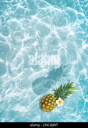 Gelbe Ananas und weiße Blume auf blauem Wasserhintergrund. Exotisches Konzept. Stockfoto