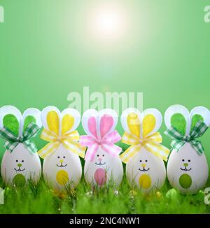 Lustige ostereier im Gras auf grünem Hintergrund. Frohe Ostergeschichte. Osterkompositionen mit süßen Kanincheneiern. Stockfoto