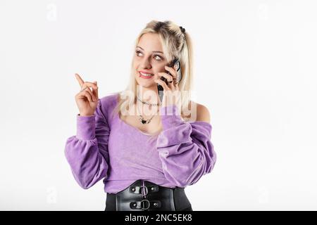 Eine blonde Frau, die isoliert auf weißem Hintergrund steht und am Telefon spricht, sich den Kopierraum ansieht und mit dem Zeigefinger zeigt. Eine Anzeige zu zeigen Stockfoto