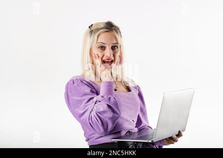 Porträt einer süßen blonden Frau, die eine Bluse trägt und isoliert auf weißem Hintergrund steht, schockiert, extrem überrascht, mit einem Notebook in Berührung kommt Stockfoto