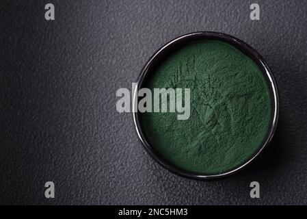 Gewürz, grüne Spirulina in Form von Pulver in einer schwarzen Schüssel auf dunklem Betonhintergrund Stockfoto