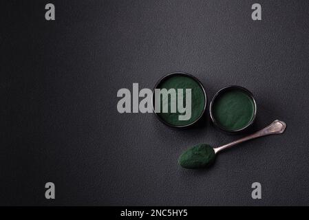 Gewürz, grüne Spirulina in Form von Pulver in einer schwarzen Schüssel auf dunklem Betonhintergrund Stockfoto