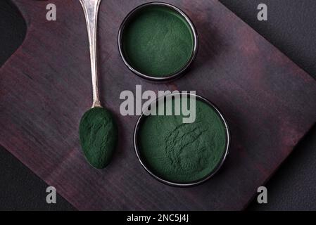 Gewürz, grüne Spirulina in Form von Pulver in einer schwarzen Schüssel auf dunklem Betonhintergrund Stockfoto