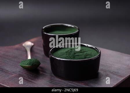 Gewürz, grüne Spirulina in Form von Pulver in einer schwarzen Schüssel auf dunklem Betonhintergrund Stockfoto