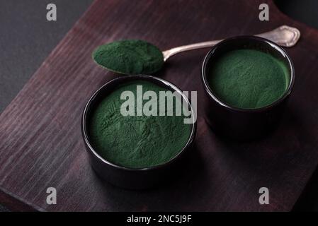 Gewürz, grüne Spirulina in Form von Pulver in einer schwarzen Schüssel auf dunklem Betonhintergrund Stockfoto