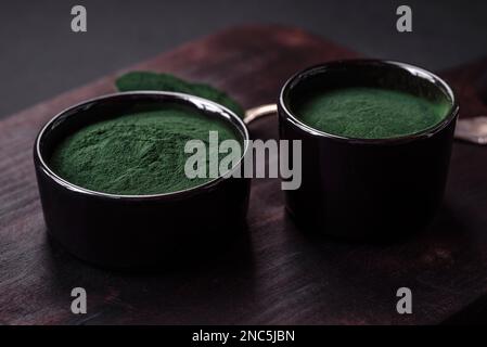 Gewürz, grüne Spirulina in Form von Pulver in einer schwarzen Schüssel auf dunklem Betonhintergrund Stockfoto