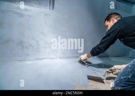 Verteilen Sie die Dämmung mit einer Kelle auf dem Betonboden Stockfoto