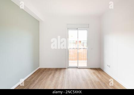 Ein leeres helles Wohnzimmer mit Zugang zum Balkon und Blick auf das Nachbarhaus. Das Zimmer verfügt über eine durchsichtige Glastür mit Zugang zum Balkon. Grau Stockfoto