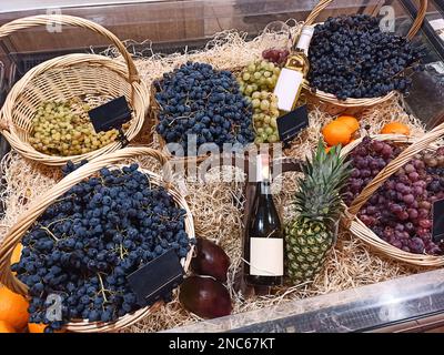 Flaschen mit unbeschrifteten Etiketten, Werbefläche und Korbkörbe mit verschiedenen Trauben in einem Weingeschäft Stockfoto