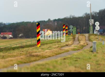 30. Januar 2023, Brandenburg, Schwedt/Oder: 30.01.2023, Schwedt/Oder. Deutsche, schwarz-rot-goldene Grenzmasten stehen auf einem Pfad nahe Schwedt an der deutsch-polnischen Grenze der oder. Dahinter befinden sich Gebäude auf polnischer Seite. (Foto mit einem starken Teleobjektiv). Foto: Wolfram Steinberg/dpa Foto: Wolfram Steinberg/dpa Stockfoto