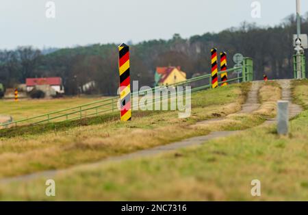 30. Januar 2023, Brandenburg, Schwedt/Oder: 30.01.2023, Schwedt/Oder. Deutsche, schwarz-rot-goldene Grenzmasten stehen auf einem Pfad nahe Schwedt an der deutsch-polnischen Grenze der oder. Dahinter befinden sich Gebäude auf polnischer Seite. (Foto mit einem starken Teleobjektiv). Foto: Wolfram Steinberg/dpa Foto: Wolfram Steinberg/dpa Stockfoto