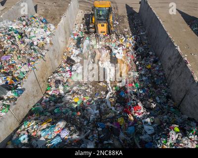 Radlader, der auf Mülldeponien eingesetzt wird, Abfallmaterial mit einer Schaufel transportiert und entsorgt, Luftaufnahme aus einem großen Winkel. Stockfoto