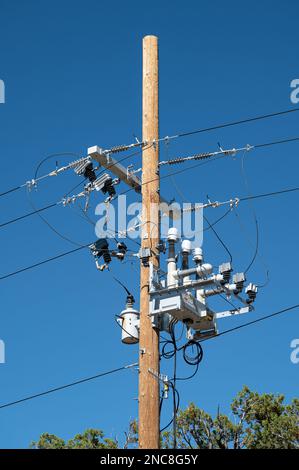 Eine vertikale Aufnahme eines alten Holzmastes, der Hochspannungskabel stützt Stockfoto