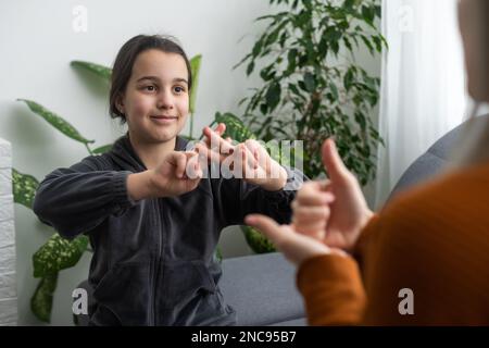 Kleines, kaukasisches Teenager-Kind Machen Sie zu Hause Artikulationsübungen mit einer fürsorglichen Mutter oder einer fürsorglichen Lehrerin. Das kleine Kind spricht Geräusche aus, spricht mit dem Lehrer oder Stockfoto