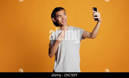 Asiatische Person, die Fotos macht und sich fröhlich benimmt, lächelt und für Bilder auf dem Smartphone posiert. Junger lächelnder Erwachsener, der Fotos auf dem Handy macht, in der Social-Media-App postet, natürlicher Look. Stockfoto