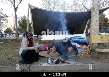 Diyarbakir, Türkei. 11. Februar 2023. Ein Paar macht Feuer, um Tee zu machen, in der Nähe einer primitiven Hütte, die sie nach dem Erdbebenwrack gebaut haben. 7 Gebäude in der Stadt wurden vollständig zerstört. Die Rettungsarbeiten in der Stadt wurden 9 Tage nach dem Erdbeben abgeschlossen. Die Zahl der Todesopfer erreichte 344. Es gibt fast 1000 Verletzte. In Diyarbakir gibt es insgesamt 307 Gebäude, von denen 26 zerstört werden, 25 sofort abgerissen werden müssen und 261 schwer beschädigt sind. Etwa 250.000 Menschen können ihr Zuhause nicht betreten. Sie leben entweder in Zeltstädten oder in sicheren Unterkünften. Einige Familien, die sagen, dass sie sich verlieben Stockfoto