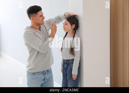 Vater misst die Körpergröße seiner Tochter an der Wand im Haus Stockfoto