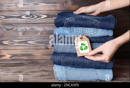 Damen- und modische Jeans mit Recycling-Etikett auf Holztisch, Nahaufnahme. Platz für Text Stockfoto