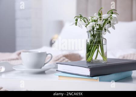 Wunderschöne Schneeglöckchen, Bücher und eine Tasse Kaffee auf dem Tablett im Schlafzimmer. Platz für Text Stockfoto