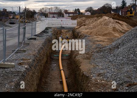 Orangefarbenes Kunststoffrohr in einem frisch gegrabenen Graben. Eingezäunte Baustelle. Stockfoto