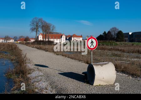 Ein Verbotsschild für Fußgänger und ein Betonring auf einem einsamen Weg, der zu einer Baustelle führt. Im Hintergrund befindet sich ein Gebäude unter einem blauen s. Stockfoto