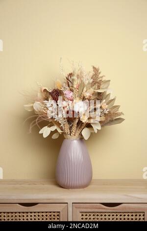 Wunderschöner getrockneter Blumenstrauß in Keramikvase auf Holztisch nahe beiger Wand Stockfoto