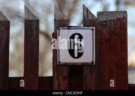 Hausnummer 6 Holzzaun mit einem metallenen Adressschild, alter rustikaler weißer Hintergrund, schwarze sechsstellige Zahl Stockfoto