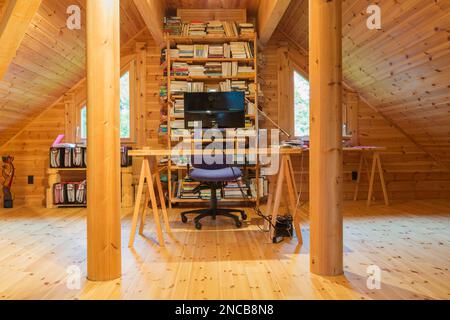 Hölzerner Schreibtischtisch mit Computer und Bücherregal im Heimbüro auf dem Zwischengeschoss in Piece sur Piece Scots Kiefernholz-Blockhaus. Stockfoto