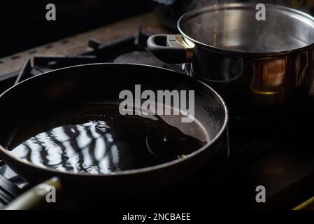 Eine mit Öl gefüllte Bratpfanne und ein Topf Wasser auf dem Herd. Vorbereitung zum Kochen. Küchenutensilien. Stockfoto