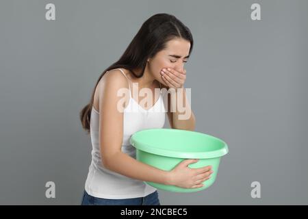 Junge Frau mit Becken mit Übelkeit auf grauem Hintergrund. Lebensmittelvergiftung Stockfoto