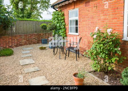 Englisches Gartenterrasse-Design. Harte Landschaftsgestaltung mit Yorker Steinsteinen in Kies und einem Bistro-Tisch mit Stühlen aus Metall. Stockfoto