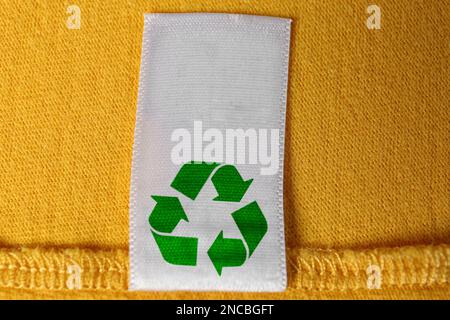 Kleidungsetikett mit Recycling-Symbol auf gelbem Pullover, Nahaufnahme Stockfoto