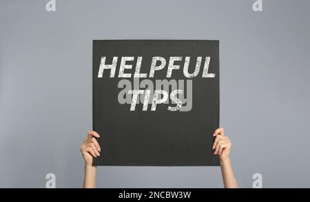 Frau mit Poster mit Satz hilfreiche Tipps auf grauem Hintergrund, Nahaufnahme Stockfoto