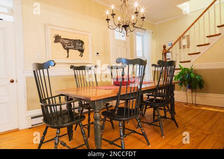 Antiker Holztisch mit hohen Windsor-Sitzsesseln im Esszimmer mit Kronleuchter und gebeizten weißen Kieferndielen im alten Haus von 1900. Stockfoto